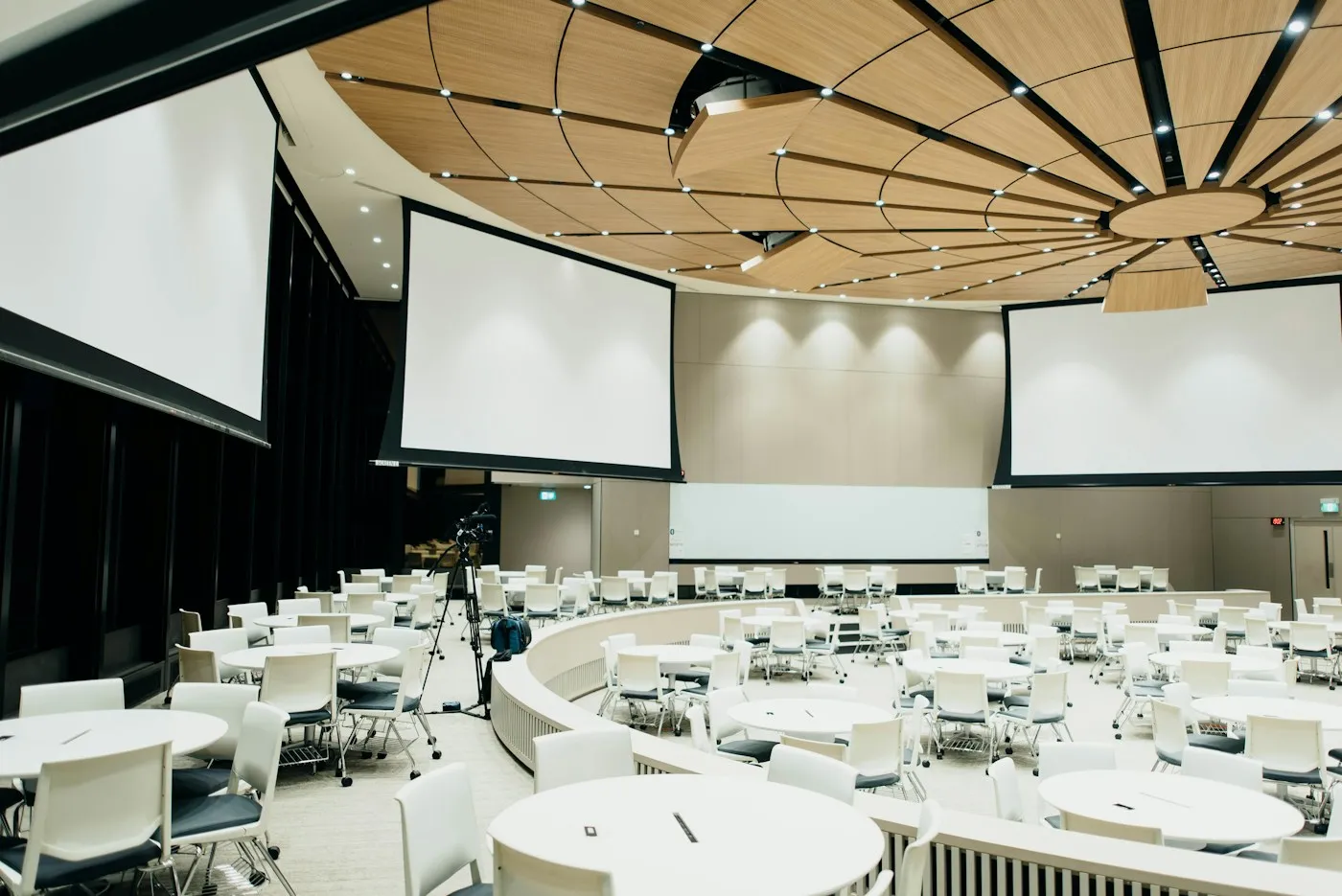 Salón de eventos con mesas redondas y pantallas de proyección listo para una conferencia