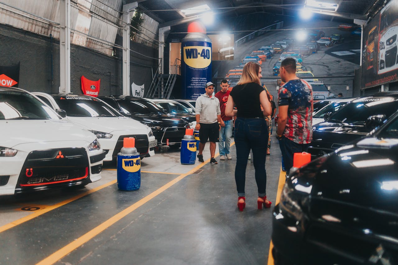 People inspecting lined-up Mitsubishi Lancer Evolutions in an indoor car show garage.