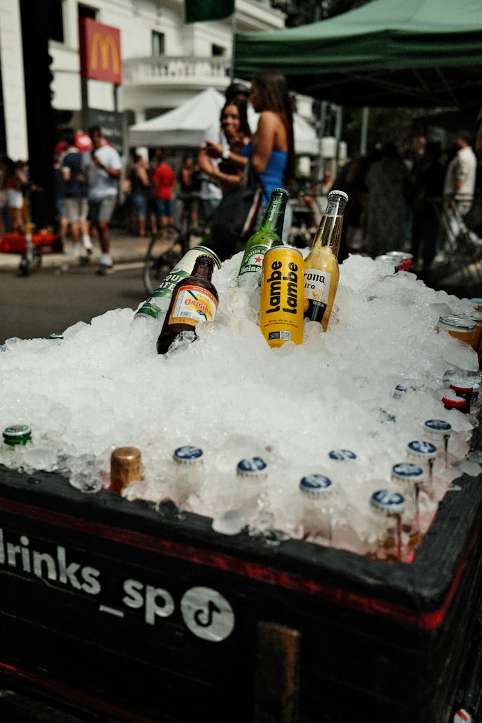 A street vendor selling various ice-cold drinks on a sunny day, with people and urban surroundings.