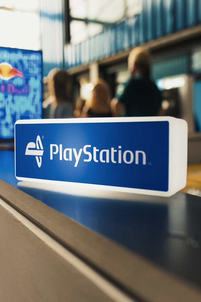 Close-up of PlayStation logo sign with blurred people in the background, indoors.